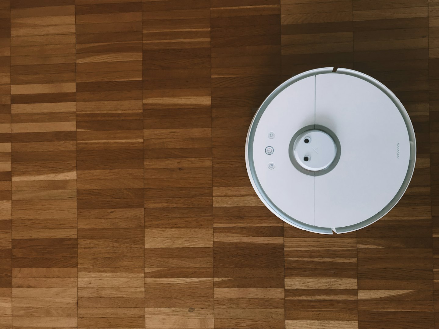 Aspirapolvere robot bianco su un pavimento in legno marrone.